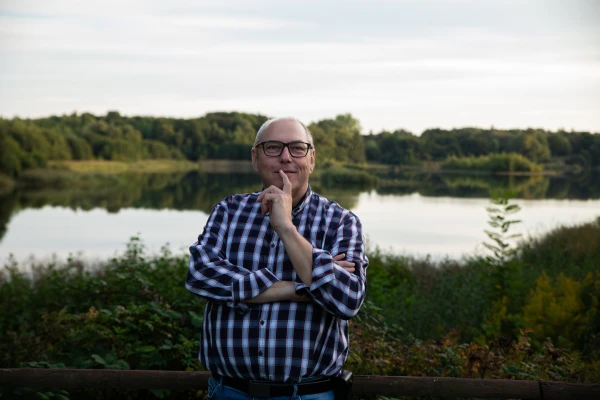 Mittelalter Mann steht vor dem See und lächelt. Sein Finger ist am Mund.